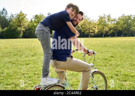 Un garçon heureux embrassant son père tout en profitant de la balade à vélo par beau temps Banque D'Images