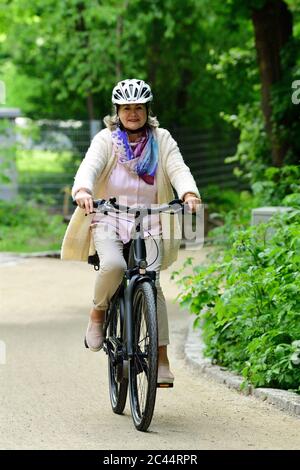 Femme aîée souriante à vélo électrique sur la piste de marche du parc Banque D'Images