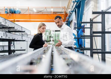 Homme d'affaires et femme examinant des tiges métalliques dans le hall de l'usine Banque D'Images