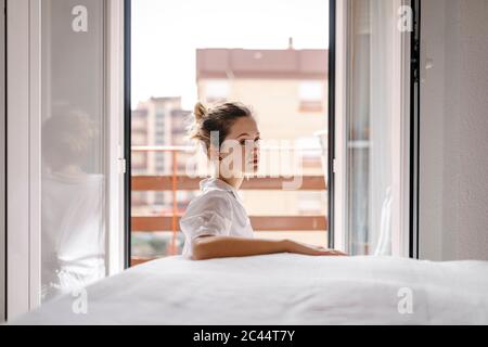 Vue latérale d'une jeune femme attentionnés qui regarde loin tout en étant assise près du lit à la maison Banque D'Images