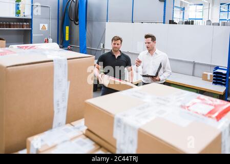 Deux hommes avec colis et presse-papiers dans la boutique d'une usine Banque D'Images