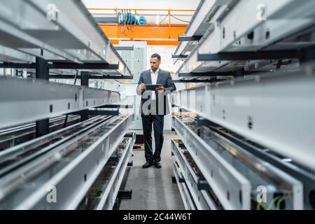 Homme d'affaires avec tablette dans des tiges métalliques dans le hall d'usine Banque D'Images