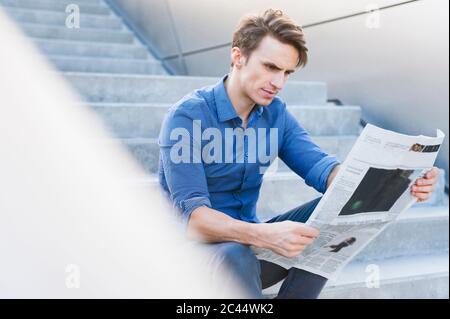 Homme d'affaires confiant et charmant lisant des journaux tout en étant assis sur les marches Banque D'Images