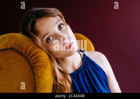 Portrait en gros plan d'une jeune femme confiante assise sur une chaise dorée sur fond magenta Banque D'Images