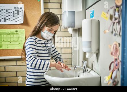 Fille portant un masque à l'école se lavant les mains Banque D'Images