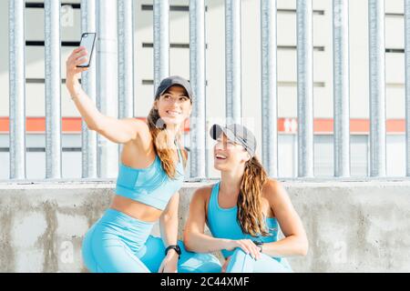 Jeune femme prenant selfie avec sœur jumelle contre la clôture de smartphone Banque D'Images
