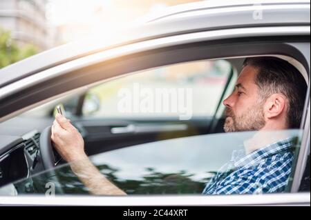 Vue latérale d'un homme charmant utilisant un téléphone portable assis en voiture Banque D'Images