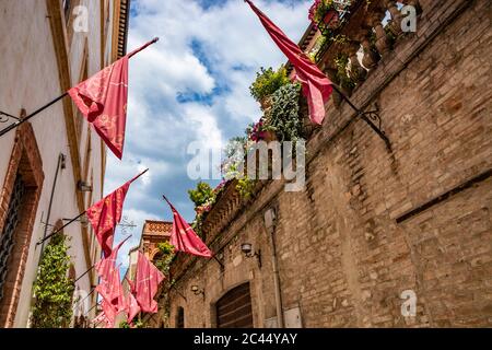 1 juin 2019 - Foligno, Pérouse, Ombrie, Italie - une ruelle dans le centre de Foligno, avec les drapeaux rouges des quartiers. Plantes et fleurs ornent le Banque D'Images