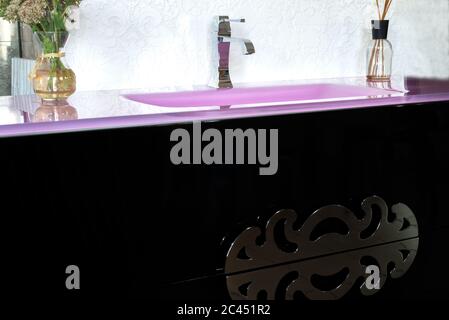 un lavabo en pierre rose brillant, dans un intérieur à la mode, avec une table de nuit en noir, avec une poignée de designer, avec des fleurs. lavabo dans le Banque D'Images