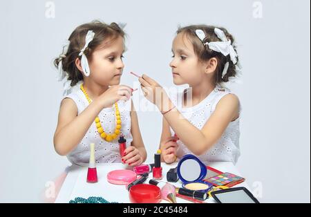 Deux petites filles jouent avec le maquillage de leur mère. Elles posent et essayent d'être des adultes.Studio, dos blanc Banque D'Images