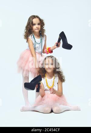 Deux petites filles jouent avec les chaussures à talons hauts de leur mère. Elles posent et essayent d'être des adultes.Studio, White back Banque D'Images