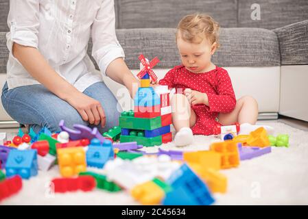 Une fille avec maman joue dans des blocs de jouets multicolores et des cubes. Banque D'Images