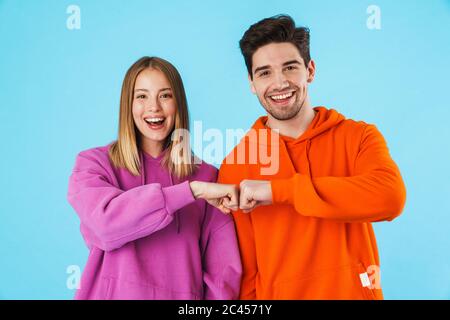 Portrait d'un jeune couple gai portant des sweats à capuche isolés sur fond bleu, poing bumping Banque D'Images