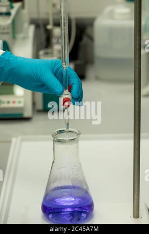 Scientifique dans un laboratoire effectuant une analyse chimique par titrage de la solution bleue. Main gantée Banque D'Images