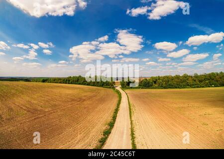 Paysage rural avec beau ciel, terres agricoles, vue aérienne. Vue de la route de terre à travers le champ labouré au printemps Banque D'Images