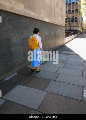 LONDRES, ROYAUME-UNI - 05 mai 2018: Une jeune fille dans une chemise blanche et une longue jupe bleue marche seule dans une rue de Londres portant un sac à dos jaune a Banque D'Images