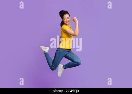 Une fille asiatique surjoyeuse sautant avec des poings surélevés sur fond de studio violet Banque D'Images