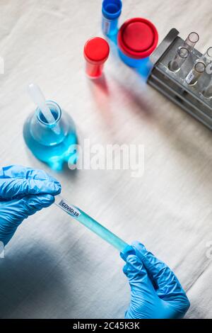 Gros plan sur les mains avec des gants portant un tube à essai Covid-19, en laboratoire. Banque D'Images