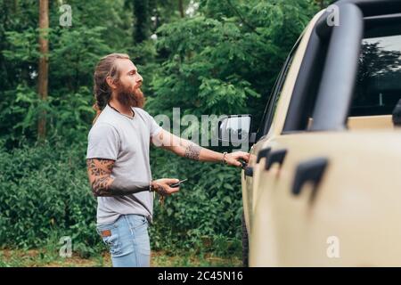 Homme tatoué barbu avec de longs cheveux de brunette entrant dans un pick-up. Banque D'Images