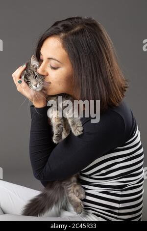 Photo studio de femme embrassant chat gris, sur fond gris. Banque D'Images
