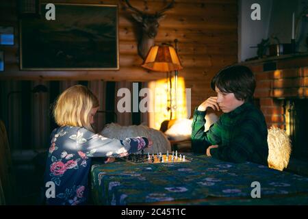 Garçon et fille assis à une table dans une cabane en rondins, jouant aux échecs, Vasterbotten LAN, Suède.