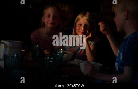 Garçon et deux filles assis à une table dans une cabane en rondins, manger, Vasterbotten LAN, Suède.