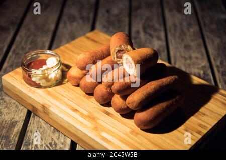 Prise de vue à angle élevé de chiens de maïs sur une planche à découper sur une surface en bois avec différentes sauces Banque D'Images