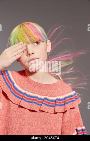 Portrait d'une fille aux cheveux longs blonds et à franges teintes portant un haut à volants roses, regardant vers le haut, sur fond gris. Banque D'Images