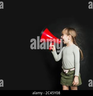 Petite fille mignonne parlant à travers un mégaphone contre un tableau noir. Enfant avec haut-parleur Banque D'Images