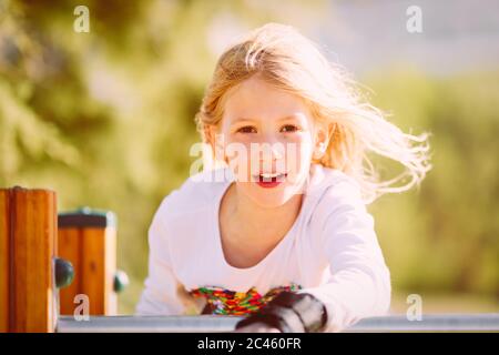 Portrait d'une petite fille mignonne, en âge d'aller à l'école primaire, avec des cheveux blonds volant dans le vent sur l'aire de jeux Banque D'Images