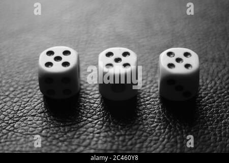 Trois dés avec cinq sur une table en cuir noir. Photo BW Banque D'Images