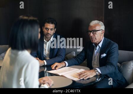 Deux hommes assis dans l'hôtel avec businesswoman Banque D'Images