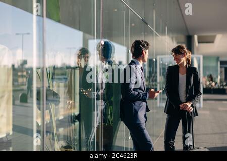 Businessman and businesswoman talking en dehors du bâtiment de verre, Malpensa, Milan Banque D'Images