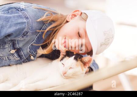 Jeune fille blonde, âge scolaire, portant une casquette solaire, caressant le chat allongé sur un lit de soleil Banque D'Images