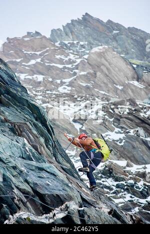 Alpiniste avec vue latérale et sac à dos avec corde fixe pour monter la haute montagne rocheuse. Homme grimpez sur la crête alpine et essayez d'atteindre le sommet de la montagne. Concept d'alpinisme et d'escalade alpine. Banque D'Images