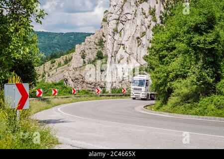 Un virage dangereux sur une route asphaltée de montagne, à gauche une série de panneaux avec des flèches rouges réfléchissantes indiquant la direction du virage. Banque D'Images