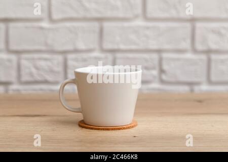 Tasse en céramique blanche pour café sur une montagne en liège sur une table en bois isolée sur une table blanche Banque D'Images