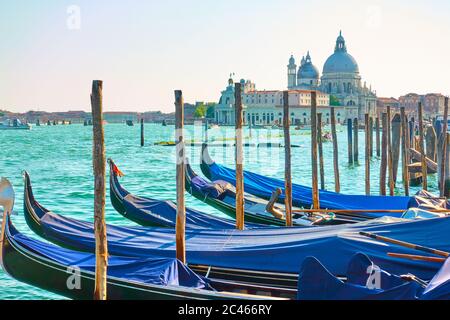 Gondoles avec des poteaux d'amarrage et église Santa Maria della Salute en arrière-plan dans la soirée, Venise, Italie. Paysage urbain vénitien Banque D'Images