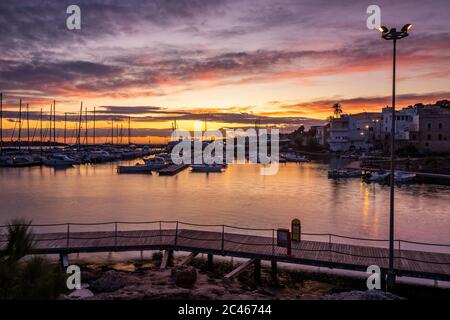 Vue sur le port touristique de Santa Maria di Leuca au coucher du soleil. Voiliers et yachts amarrés sur les quais du port. Des allées en bois mènent au port qua Banque D'Images