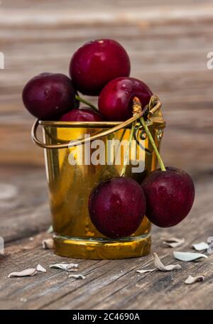 Baies de cerises rouges mûres avec gouttes d'eau sur elles gros plan dans un seau en métal sur une surface en bois Banque D'Images