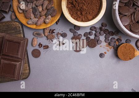 Morceaux et gouttes de chocolat, fèves de cacao et poudre sur fond gris Banque D'Images