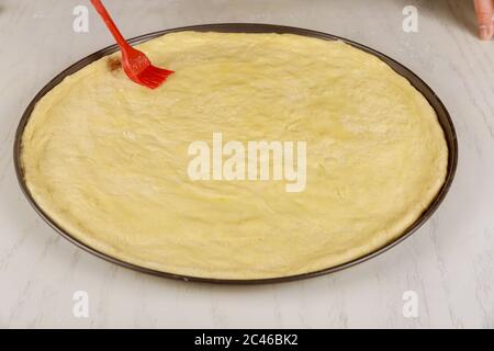 Préparation de la pâte pour faire une pizza ronde sur une table blanche. Banque D'Images