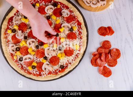 Femme mettant des tranches d'olives sur de la pâte à pizza crue. Banque D'Images