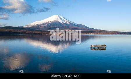 Photo aérienne du Mont Fuji avec sa casquette de neige et le calme lac Yamanaka au Japon, un matin d'hiver avec un ferry touristique en premier plan Banque D'Images