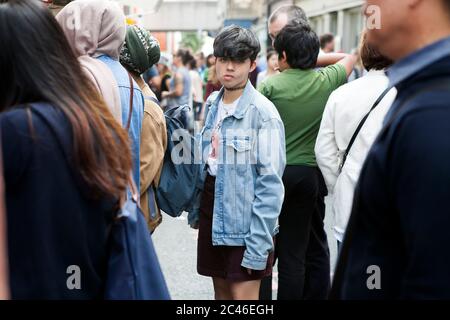 Londres, Royaume-Uni - 17 juillet 2019, UNE fille brune à poil court avec une chaîne autour de son cou, dans une jupe noire courte, un T-shirt blanc et une snea veste bleue en denim Banque D'Images