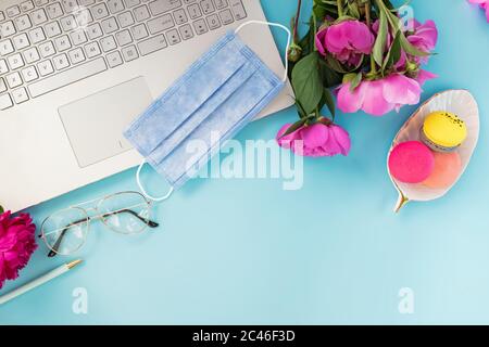 Composition de la couche plate avec lyine masque médical sur l'ordinateur portable, café et pivoines sur fond bleu. Banque D'Images