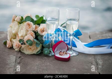 Des verres de bouquet de champagne de roses et une paire d'anneaux dorés se trouvent sur le carrelage en pierre Banque D'Images