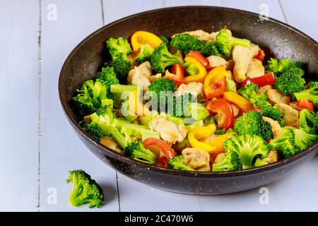 Sautés sains et savoureux, faites frire les légumes avec du poulet dans une casserole sur une surface en bois blanc. Banque D'Images