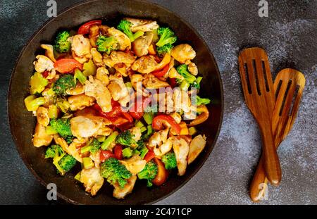 Poulet sauté au brocoli, poivron rouge et jaune sur fond sombre. Gros plan. Banque D'Images