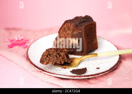 Une tranche d'un gâteau au chocolat avec des pommes sur une assiette blanche, un morceau de gâteau sur une fourchette d'or près. Serviette et arrière-plan roses. Banque D'Images